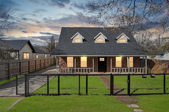 cape cod home featuring brick siding, a fenced front yard, covered porch, and a yard