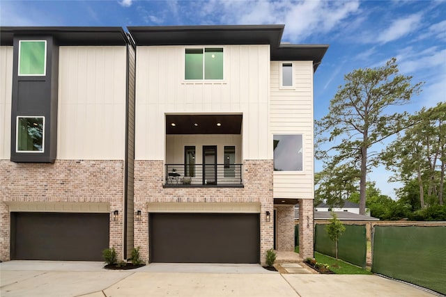 view of front of house featuring a garage, concrete driveway, brick siding, and a balcony