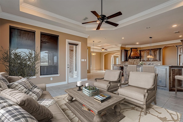 living area with light tile patterned floors, visible vents, arched walkways, a raised ceiling, and crown molding
