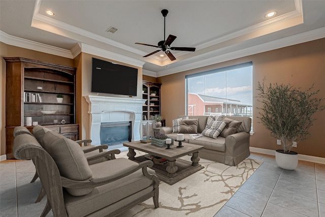 living area featuring ornamental molding, a glass covered fireplace, a raised ceiling, and visible vents