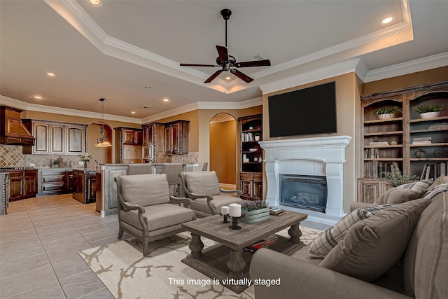 living area with arched walkways, a tray ceiling, light tile patterned flooring, and crown molding