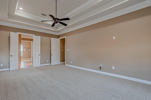 unfurnished bedroom featuring a tray ceiling, light colored carpet, visible vents, and baseboards
