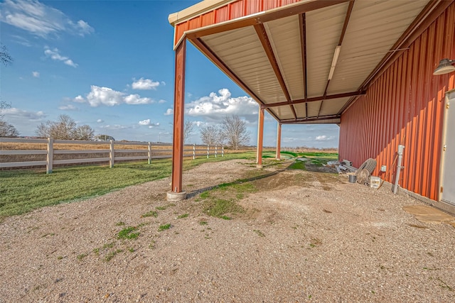 view of yard with an attached carport, a rural view, and fence