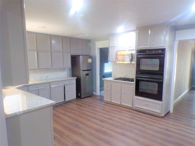 kitchen featuring black appliances, dark wood finished floors, light stone countertops, and decorative backsplash