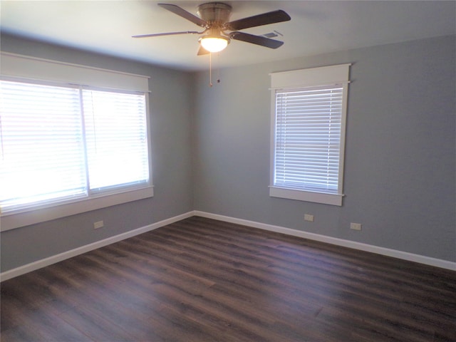 spare room featuring dark wood-style floors, a ceiling fan, visible vents, and baseboards