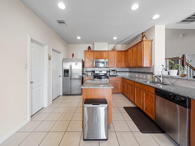 kitchen featuring appliances with stainless steel finishes, stone countertops, a center island, and a sink