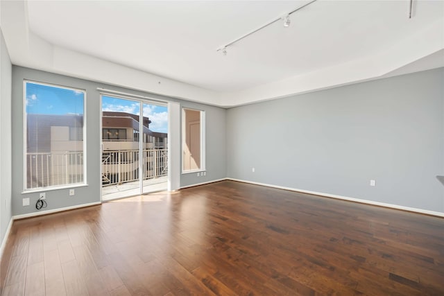 empty room with rail lighting, baseboards, and wood finished floors