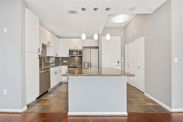 kitchen featuring stainless steel appliances, a kitchen island, white cabinetry, visible vents, and decorative backsplash