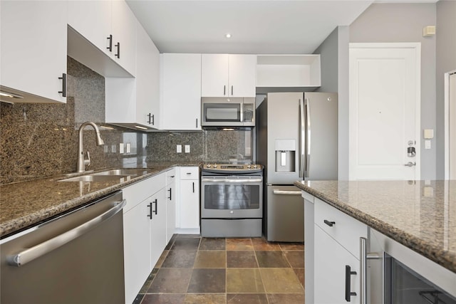 kitchen with stainless steel appliances, a sink, white cabinetry, dark stone counters, and tasteful backsplash