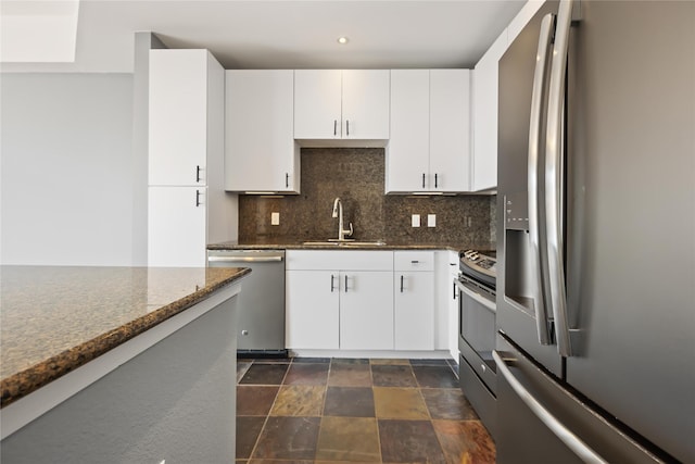 kitchen with backsplash, appliances with stainless steel finishes, white cabinets, a sink, and dark stone counters