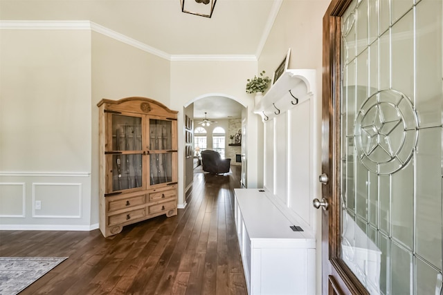 foyer with arched walkways, dark wood finished floors, wainscoting, crown molding, and a decorative wall