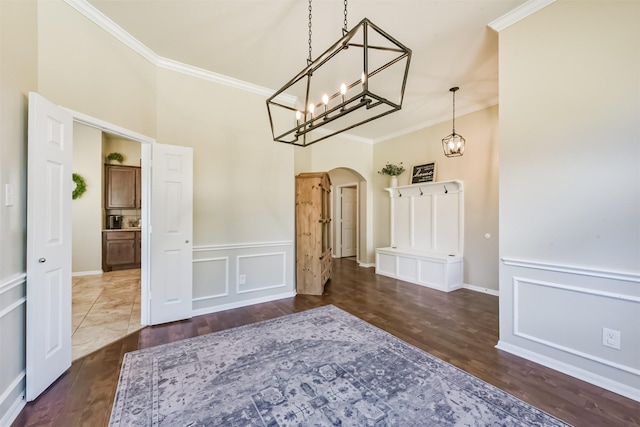 unfurnished dining area with arched walkways, a decorative wall, ornamental molding, wainscoting, and wood finished floors