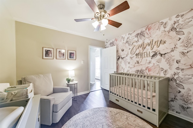 bedroom featuring baseboards, a crib, dark wood-style flooring, and wallpapered walls