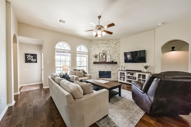 living room with ceiling fan, a fireplace, visible vents, baseboards, and dark wood finished floors