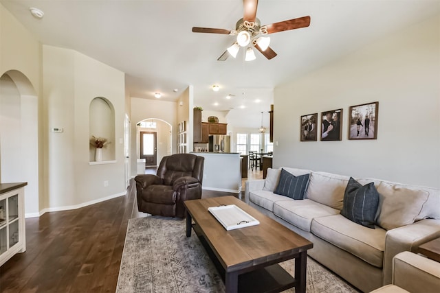 living area with baseboards, arched walkways, ceiling fan, and dark wood-style flooring