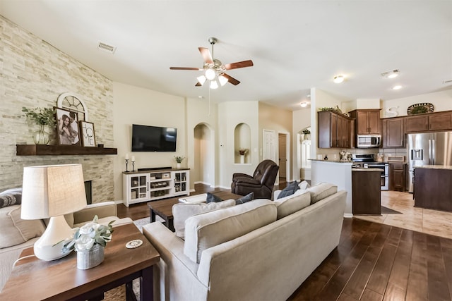 living area with arched walkways, a fireplace, visible vents, ceiling fan, and wood finished floors