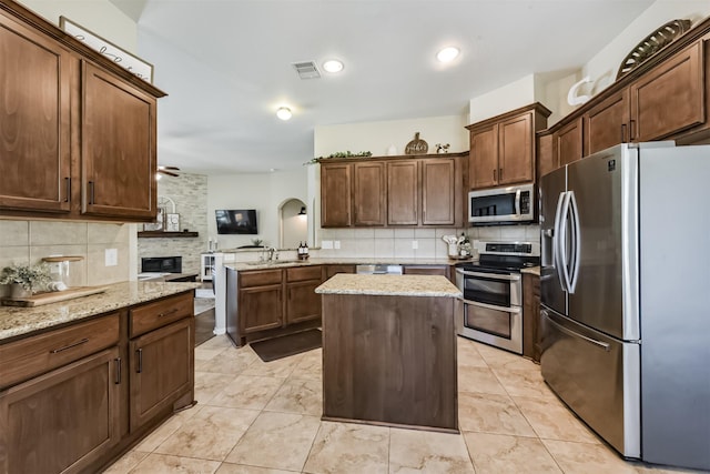 kitchen featuring light stone counters, visible vents, appliances with stainless steel finishes, a center island, and tasteful backsplash