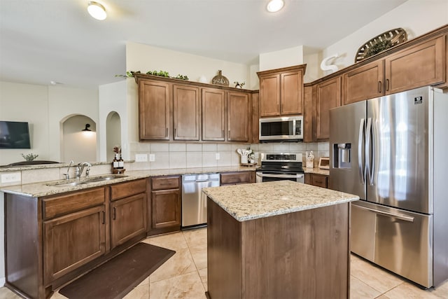 kitchen featuring tasteful backsplash, appliances with stainless steel finishes, a sink, light stone countertops, and a peninsula