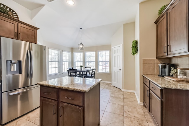 kitchen featuring tasteful backsplash, stainless steel fridge with ice dispenser, decorative light fixtures, light stone countertops, and vaulted ceiling