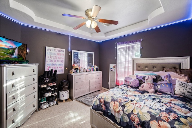 carpeted bedroom with a raised ceiling and ceiling fan