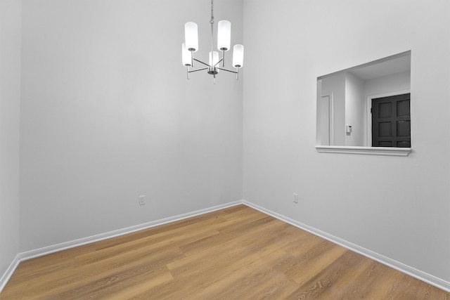 empty room featuring a chandelier, baseboards, and wood finished floors