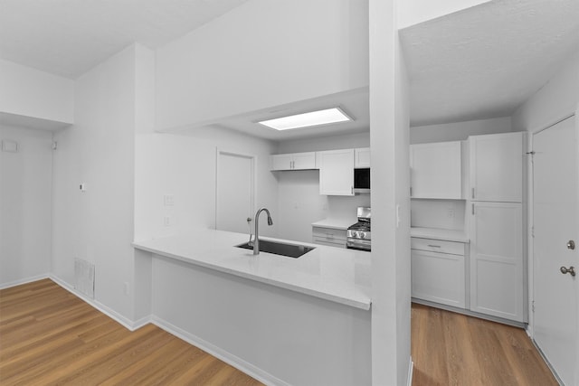 kitchen with stainless steel gas range oven, white cabinets, wood finished floors, light countertops, and a sink