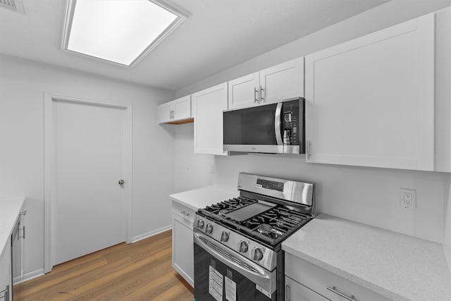 kitchen with light countertops, appliances with stainless steel finishes, white cabinetry, and light wood-style floors