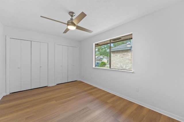 unfurnished bedroom with light wood finished floors, a ceiling fan, baseboards, and two closets