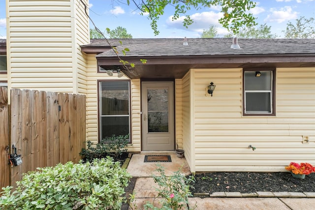 doorway to property featuring roof with shingles and fence