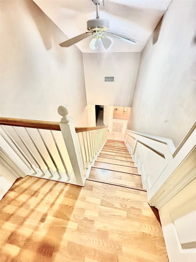 staircase featuring wood finished floors, visible vents, and a ceiling fan