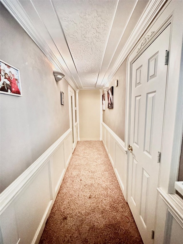 corridor featuring a textured ceiling, ornamental molding, a decorative wall, and carpet flooring