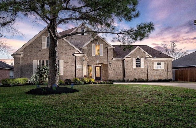 traditional-style home with brick siding, fence, and a front lawn