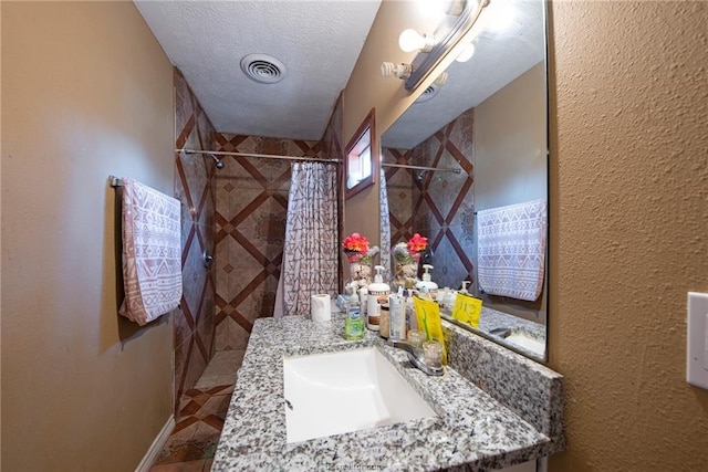 full bathroom featuring visible vents, a textured wall, a textured ceiling, vanity, and tiled shower