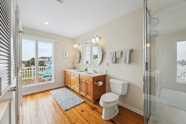 bathroom with hardwood / wood-style floors, toilet, a shower with shower door, a sink, and baseboards