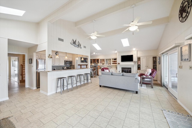 living area with a ceiling fan, a skylight, a glass covered fireplace, and beamed ceiling