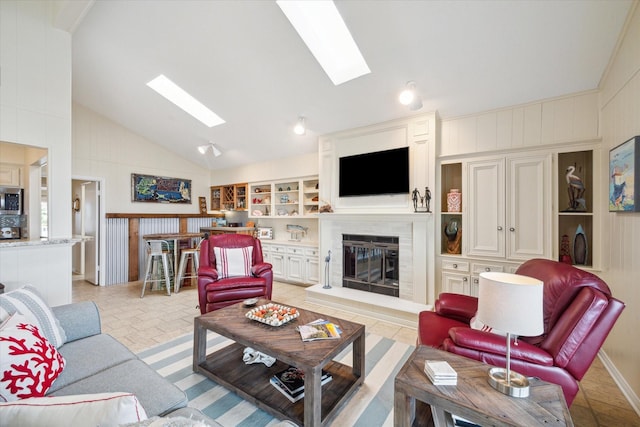 living room featuring built in shelves, a skylight, a glass covered fireplace, and high vaulted ceiling