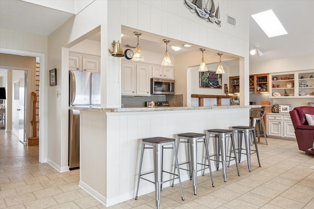 kitchen with a skylight, tasteful backsplash, visible vents, appliances with stainless steel finishes, and a kitchen breakfast bar