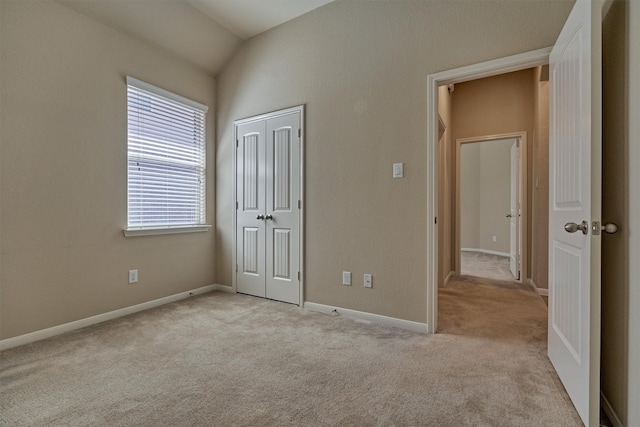 unfurnished bedroom featuring lofted ceiling, a closet, carpet flooring, and baseboards