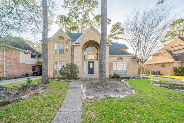 view of front of home with driveway, brick siding, a front lawn, and central AC unit