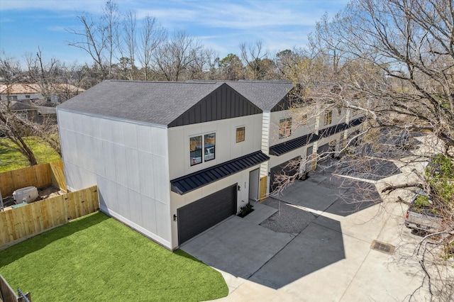 view of side of property with an attached garage, a shingled roof, fence, concrete driveway, and board and batten siding