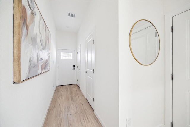 hall featuring light wood-style flooring, visible vents, and baseboards