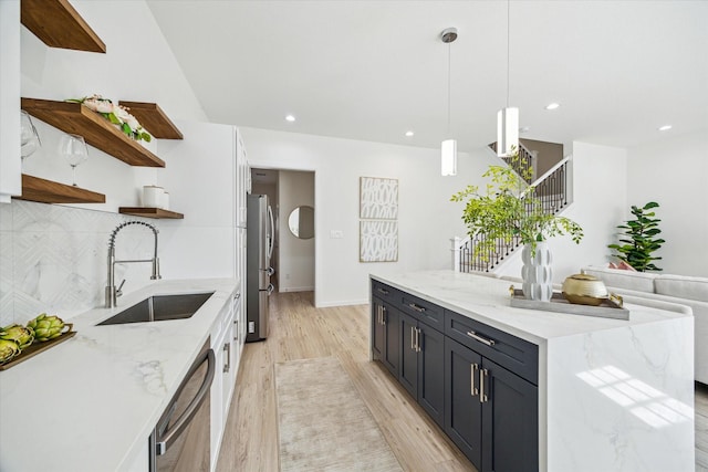 kitchen with light wood finished floors, open shelves, stainless steel appliances, decorative backsplash, and a sink