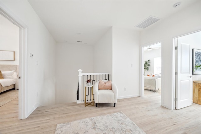 sitting room with baseboards, visible vents, an upstairs landing, and wood finished floors