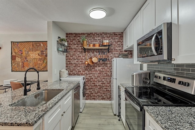 kitchen with stone countertops, appliances with stainless steel finishes, a sink, white cabinetry, and backsplash