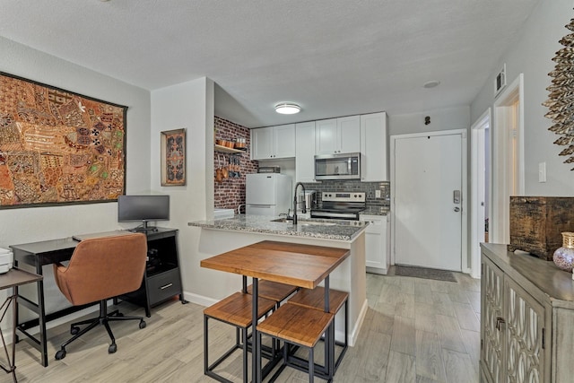 kitchen with stainless steel appliances, a peninsula, a sink, decorative backsplash, and light wood finished floors