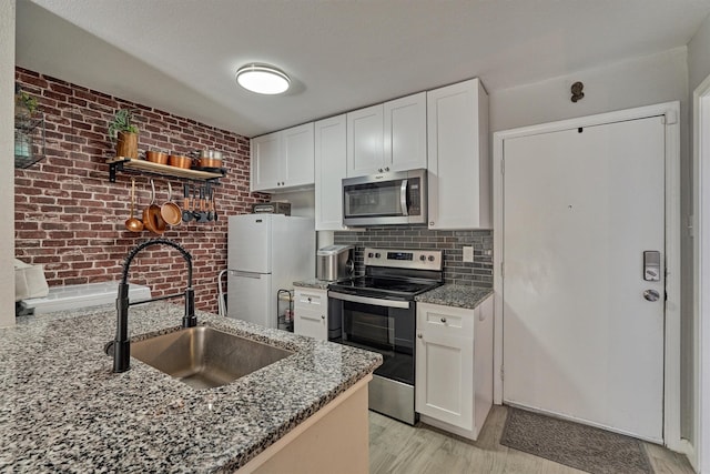 kitchen featuring stainless steel appliances, stone counters, white cabinets, and a sink