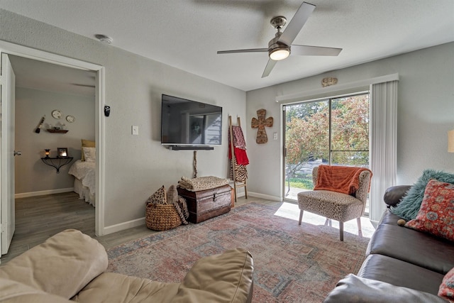 living area with a ceiling fan, a textured ceiling, baseboards, and wood finished floors