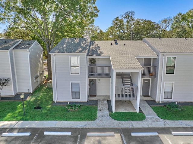 view of property with uncovered parking, a front yard, roof with shingles, and a balcony