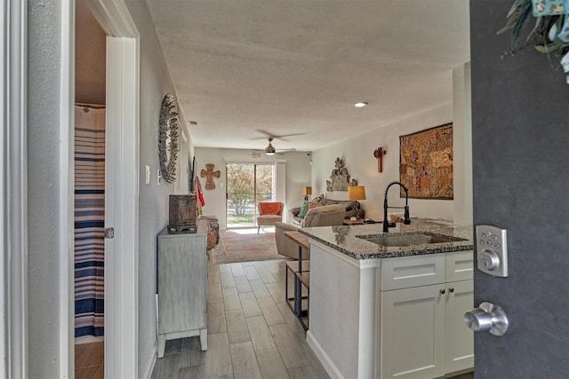 kitchen with wood finish floors, open floor plan, white cabinets, a sink, and dark stone counters