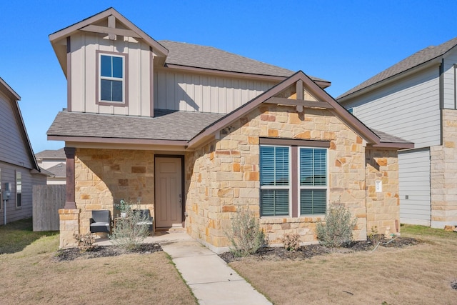 view of front of home with board and batten siding, a front yard, stone siding, and roof with shingles